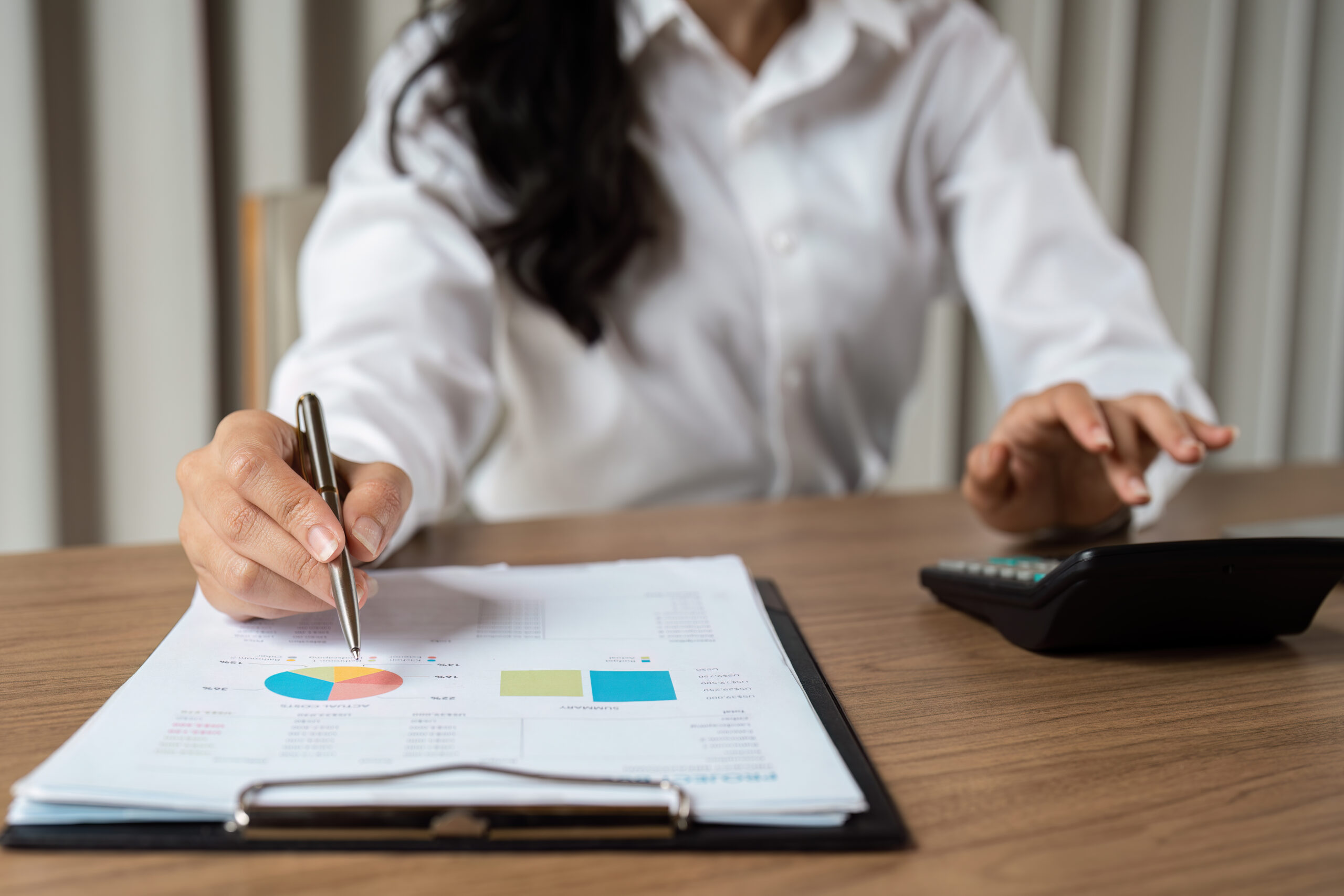 Professional woman reviewing financial charts and using a calculator, focusing on business analysis and strategic planning.